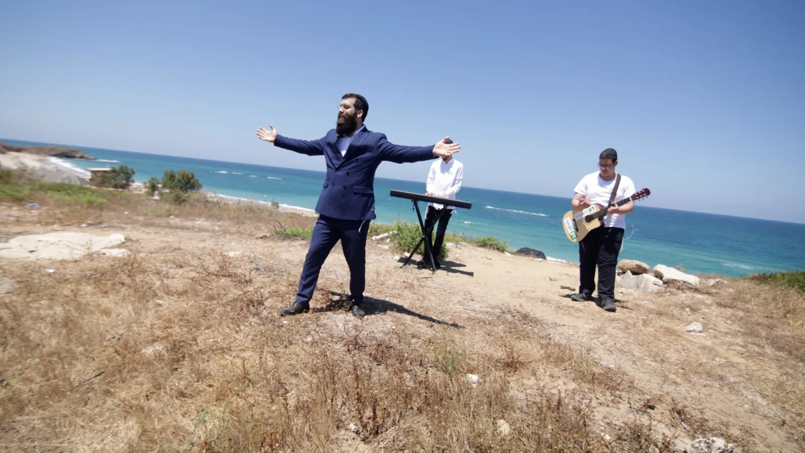 זמר ושני נגנים מנגנים על צוק מול הים